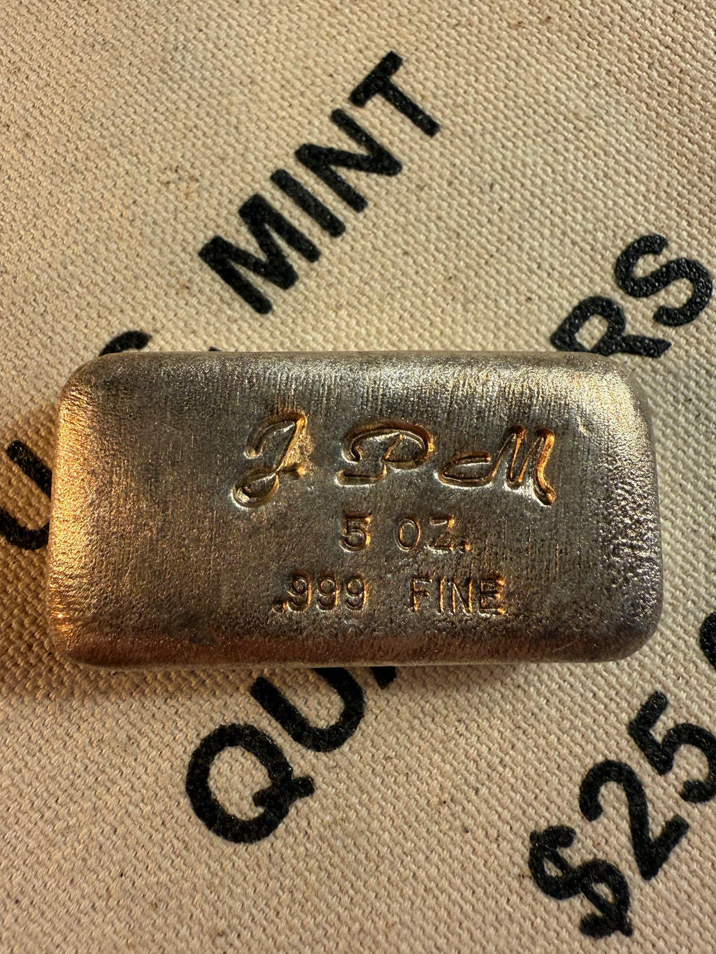 Jackson Precious Metals JPM 5 oz .999 fine silver hand-poured loaf bar with script JPM hallmark, displayed on vintage U.S. Mint quarters bag.